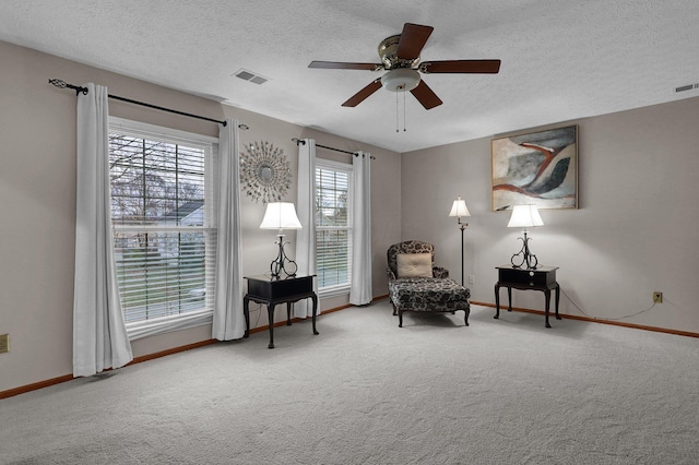 living area featuring carpet floors, a textured ceiling, baseboards, visible vents, and ceiling fan