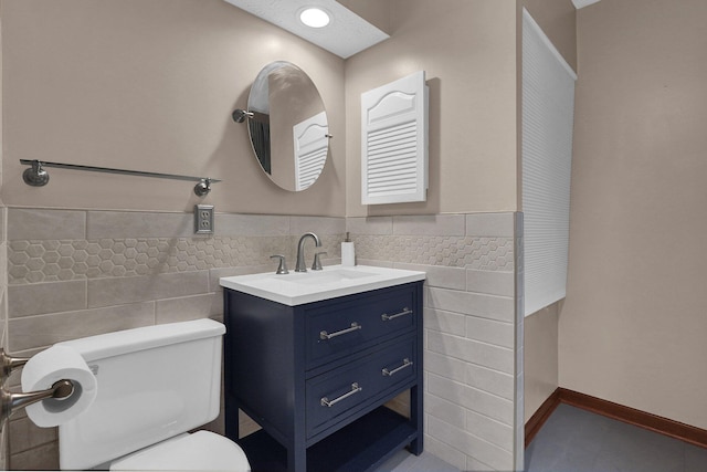 bathroom featuring tile walls, toilet, vanity, and wainscoting