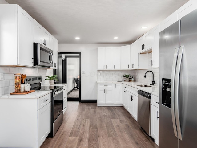 kitchen with backsplash, white cabinets, sink, wood-type flooring, and stainless steel appliances