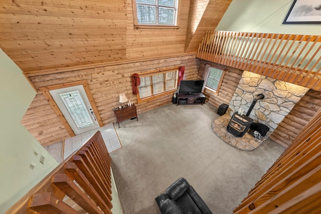 carpeted living room with a wood stove, a towering ceiling, and wooden ceiling