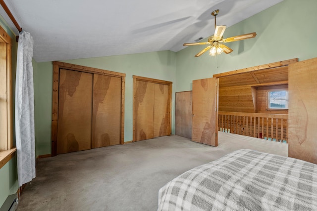 bedroom with light carpet, vaulted ceiling, baseboard heating, ceiling fan, and multiple closets