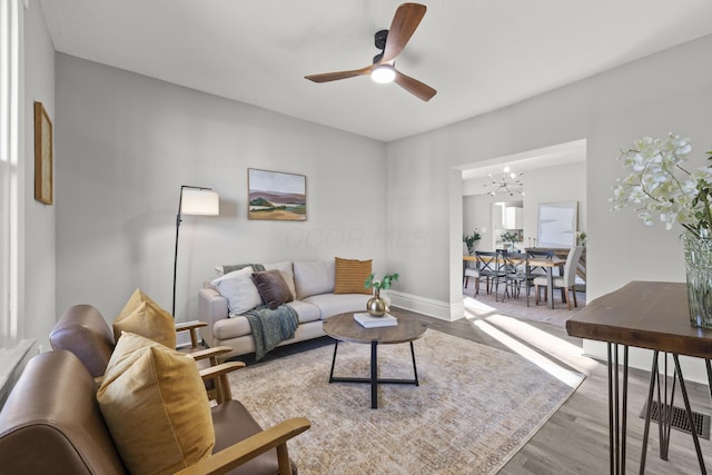 living room featuring ceiling fan with notable chandelier and light hardwood / wood-style flooring