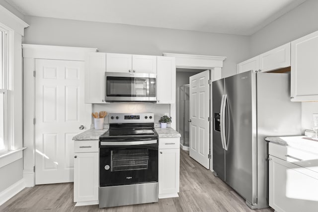 kitchen with light stone countertops, light hardwood / wood-style flooring, white cabinets, and stainless steel appliances