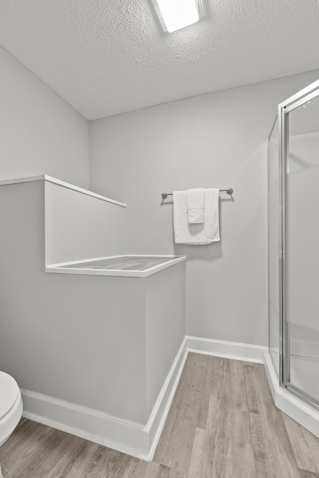 bathroom with a shower with door, wood-type flooring, a textured ceiling, and toilet