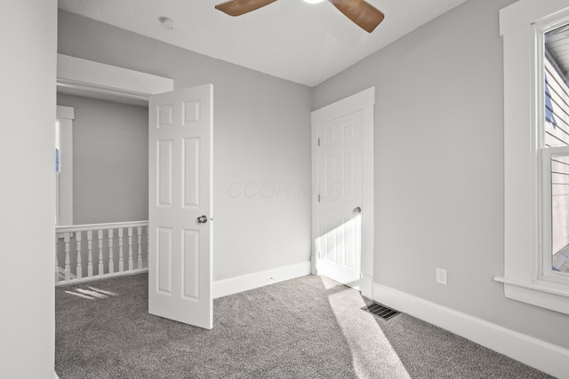 unfurnished bedroom featuring ceiling fan, a nursery area, and dark carpet