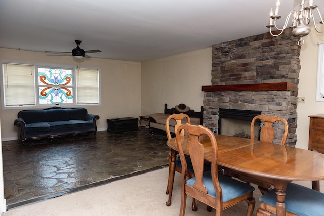 dining space featuring a stone fireplace, ceiling fan with notable chandelier, and concrete floors