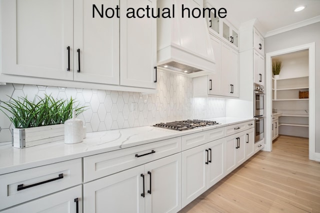 kitchen featuring premium range hood, white cabinets, light hardwood / wood-style flooring, light stone countertops, and tasteful backsplash