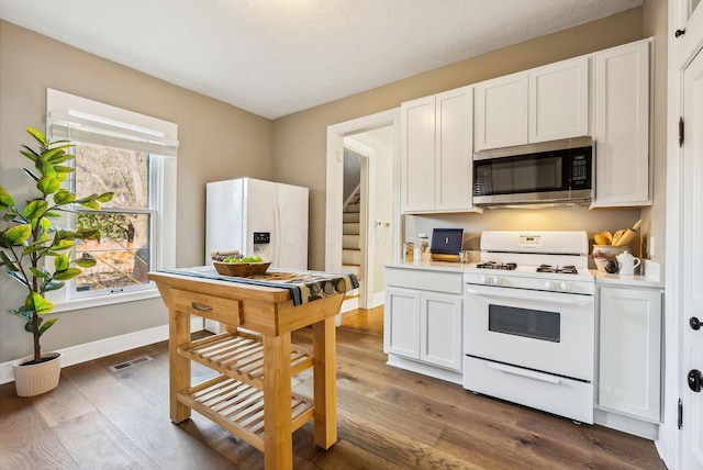 kitchen featuring a textured ceiling, white cabinetry, wood-type flooring, and white appliances