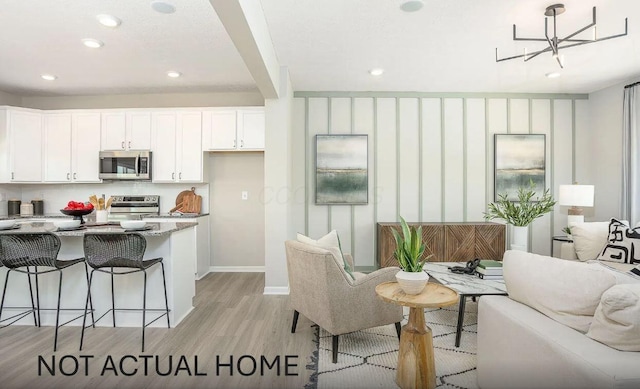 kitchen featuring a breakfast bar area, light wood-type flooring, appliances with stainless steel finishes, light stone countertops, and white cabinets