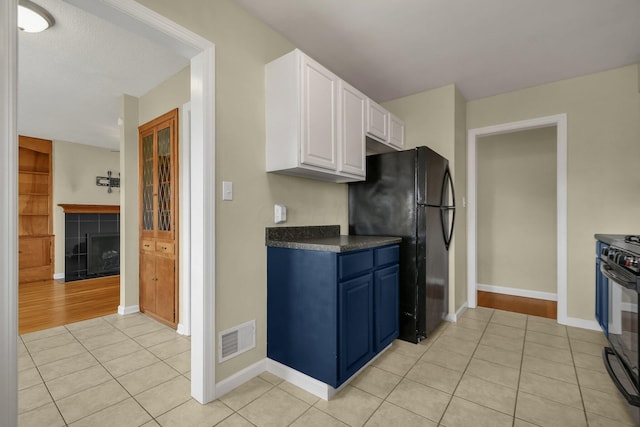 kitchen featuring white cabinets, light tile patterned flooring, a tiled fireplace, and black appliances