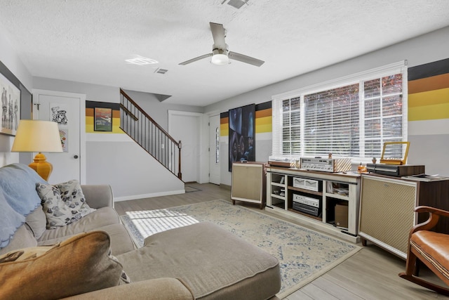 living room with ceiling fan, light wood-type flooring, and a textured ceiling