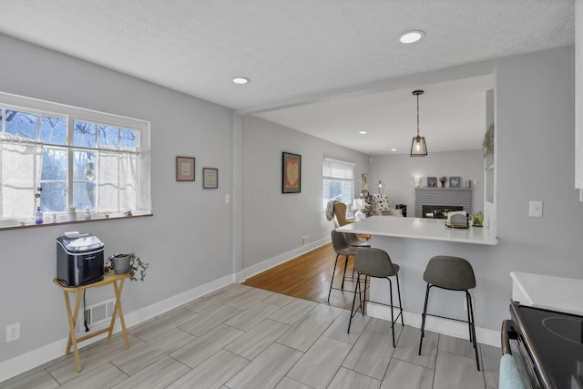 kitchen with kitchen peninsula, a textured ceiling, decorative light fixtures, a breakfast bar area, and a fireplace