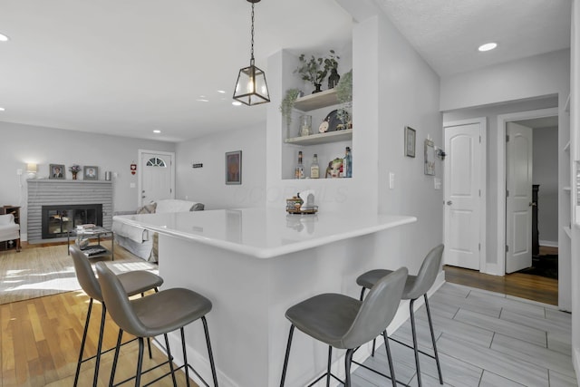 kitchen featuring a kitchen breakfast bar, kitchen peninsula, a fireplace, and light hardwood / wood-style flooring