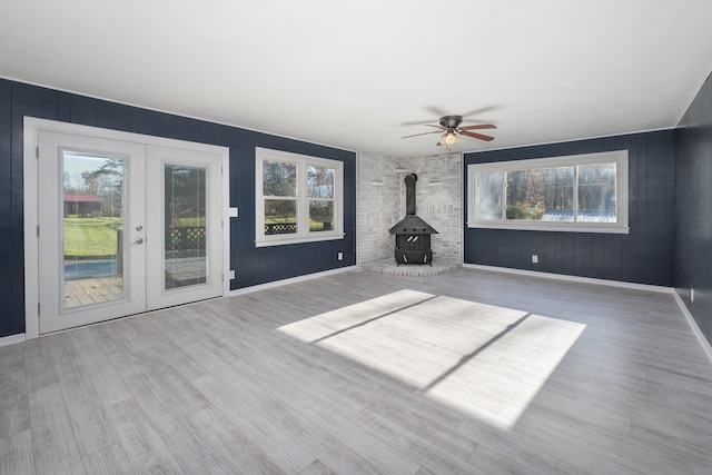 unfurnished living room with french doors, light hardwood / wood-style floors, a wood stove, and ceiling fan