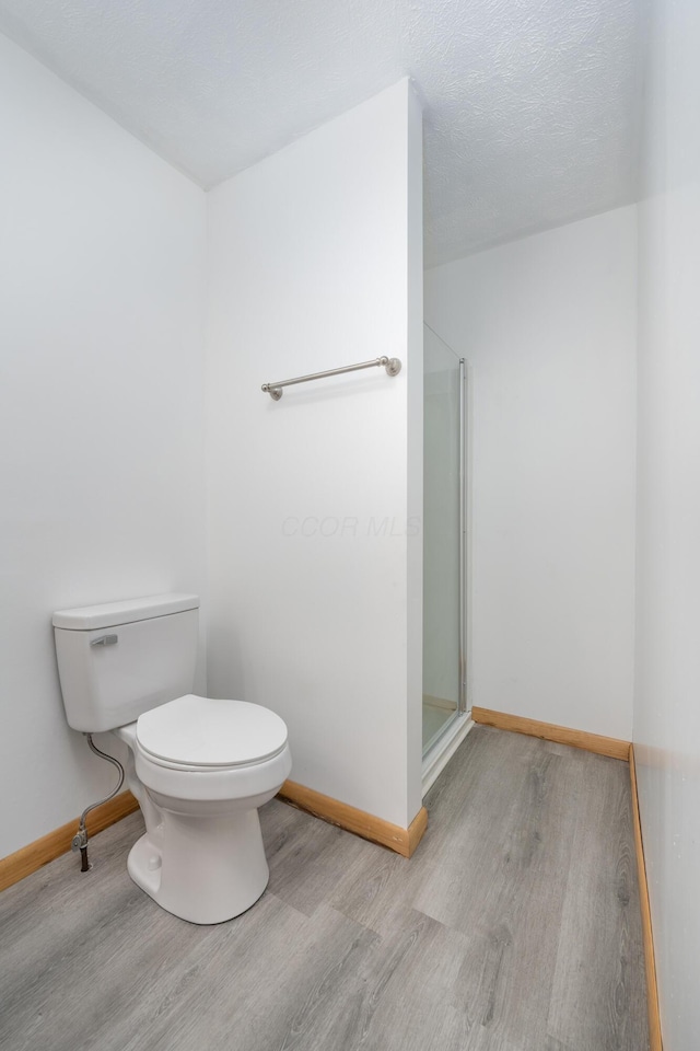 bathroom featuring wood-type flooring, a textured ceiling, toilet, and a shower with shower door