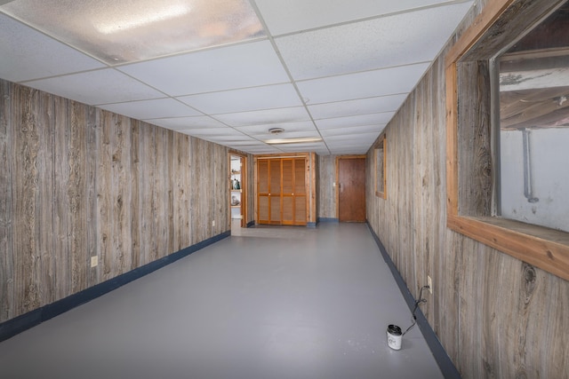 basement with a paneled ceiling and wood walls