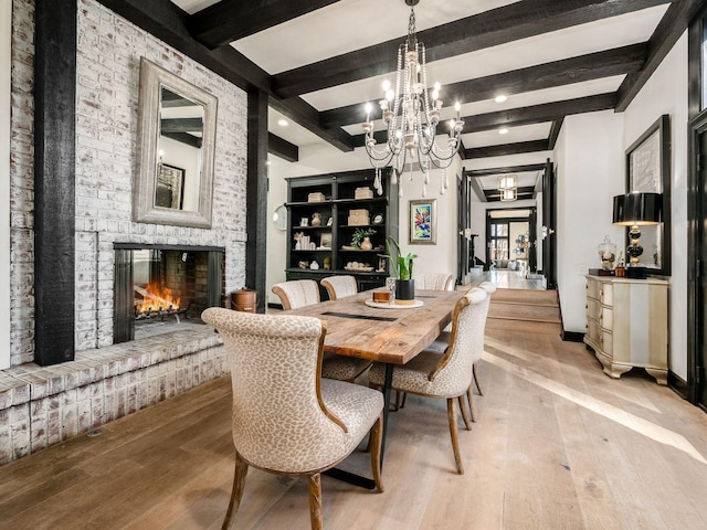 dining area featuring beamed ceiling, light hardwood / wood-style floors, an inviting chandelier, and a brick fireplace