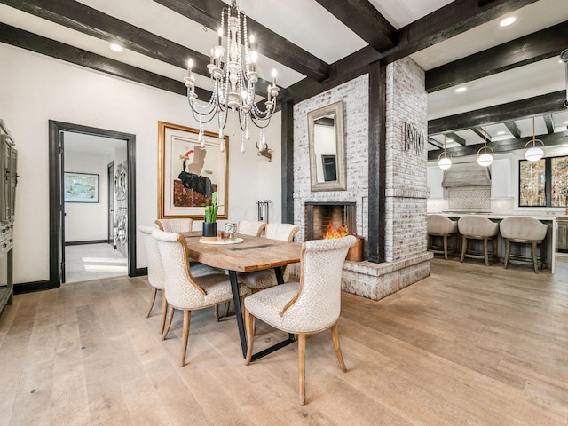 dining area with beam ceiling, a brick fireplace, a notable chandelier, and light wood-type flooring