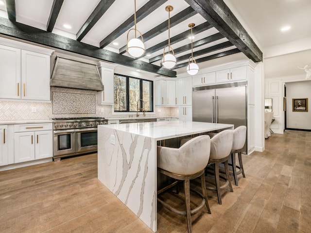 kitchen featuring high end appliances, white cabinetry, hanging light fixtures, backsplash, and custom exhaust hood