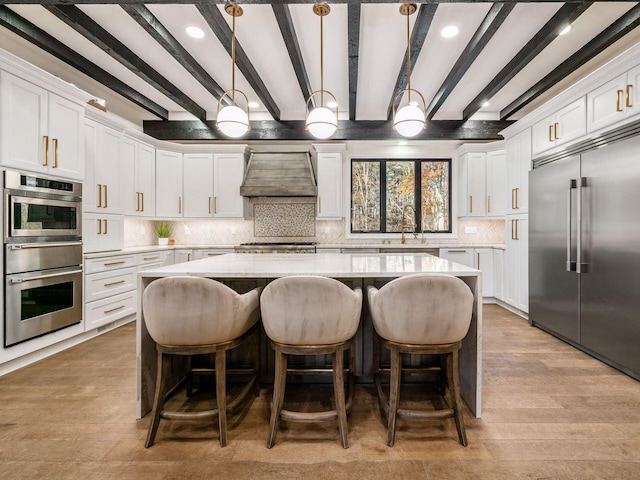 kitchen featuring beam ceiling, hanging light fixtures, backsplash, custom range hood, and appliances with stainless steel finishes