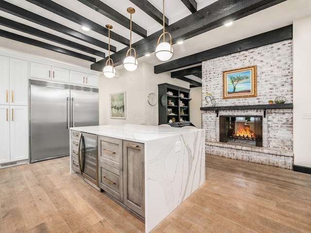 kitchen with beam ceiling, light stone countertops, hanging light fixtures, built in refrigerator, and white cabinets