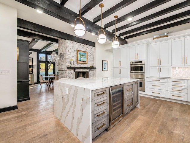 kitchen with pendant lighting, a spacious island, light stone counters, white cabinetry, and beverage cooler