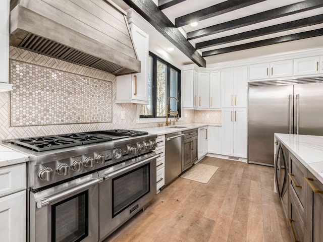 kitchen with light stone counters, custom range hood, high quality appliances, white cabinets, and light hardwood / wood-style floors