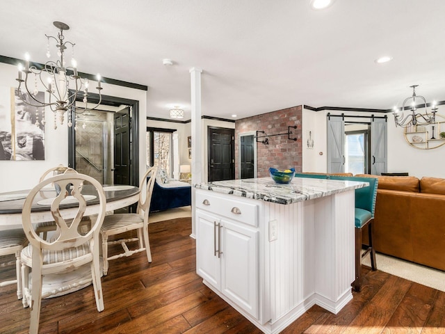 kitchen with light stone countertops, a barn door, decorative light fixtures, dark hardwood / wood-style floors, and white cabinetry