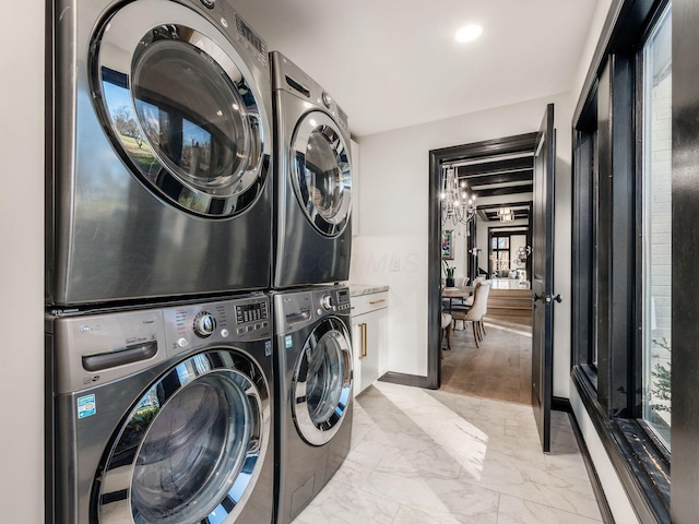 clothes washing area featuring a chandelier, light wood-type flooring, stacked washing maching and dryer, and cabinets