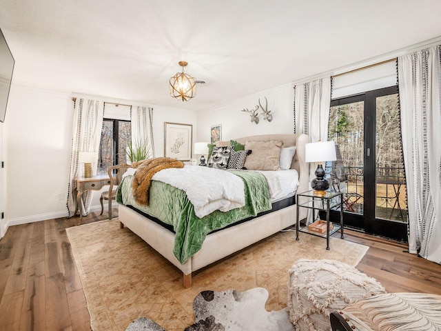 bedroom with access to outside, multiple windows, hardwood / wood-style floors, and an inviting chandelier