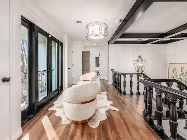 hallway with light hardwood / wood-style floors, an inviting chandelier, beam ceiling, and french doors