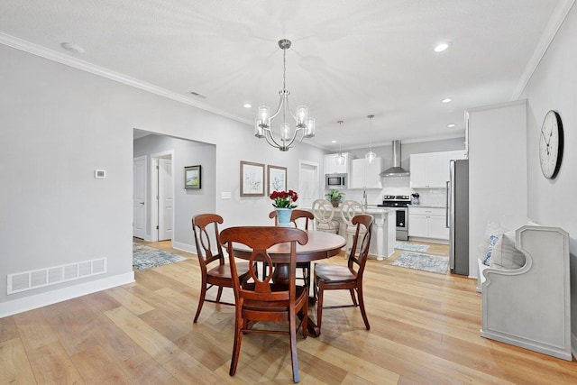 dining area featuring light hardwood / wood-style floors, ornamental molding, a textured ceiling, and an inviting chandelier