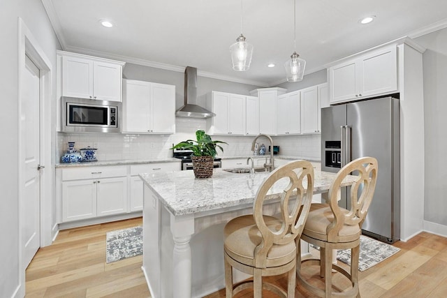 kitchen featuring appliances with stainless steel finishes, wall chimney exhaust hood, sink, a center island with sink, and light hardwood / wood-style flooring