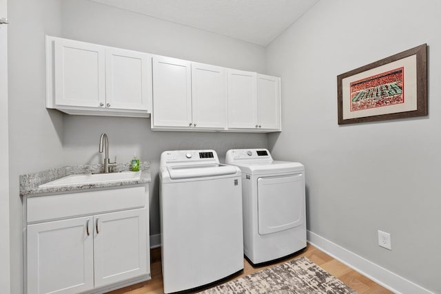 washroom with cabinets, a textured ceiling, sink, washing machine and dryer, and light hardwood / wood-style floors