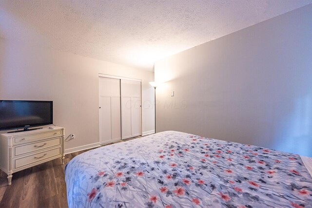 bedroom with a textured ceiling, dark wood-type flooring, and a closet