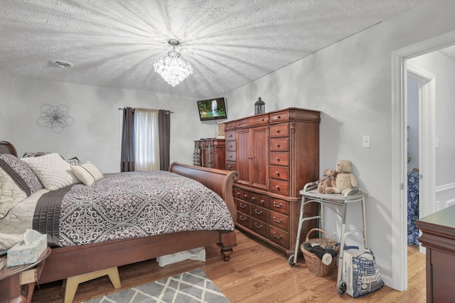 bedroom with a textured ceiling, light hardwood / wood-style floors, and an inviting chandelier