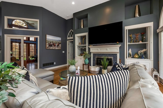 living room with a high end fireplace, french doors, a high ceiling, built in features, and hardwood / wood-style floors