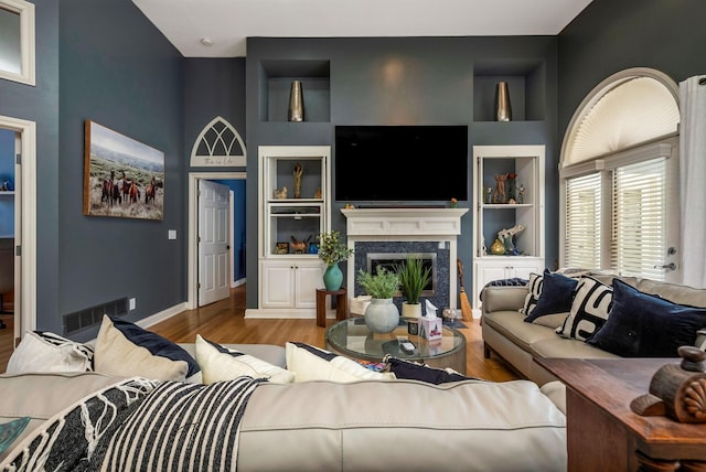 living room featuring built in shelves, hardwood / wood-style flooring, a high ceiling, and a premium fireplace