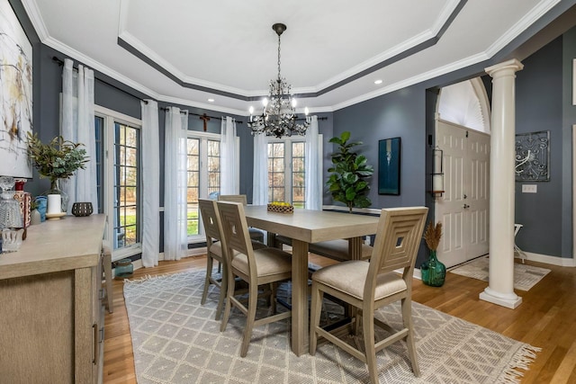 dining room featuring a raised ceiling, ornate columns, light hardwood / wood-style floors, and ornamental molding