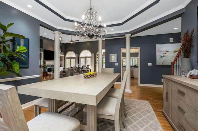 dining room featuring a tray ceiling, ornate columns, ornamental molding, and light wood-type flooring