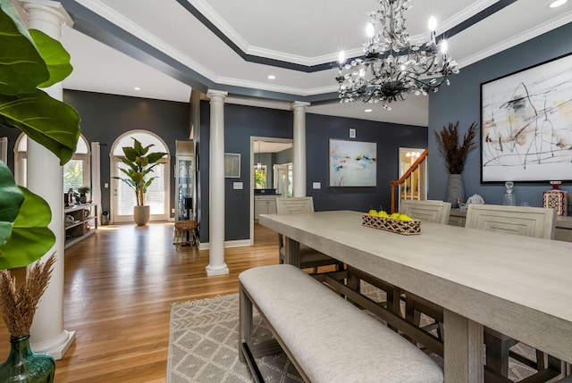 dining space featuring decorative columns, wood-type flooring, a notable chandelier, and ornamental molding