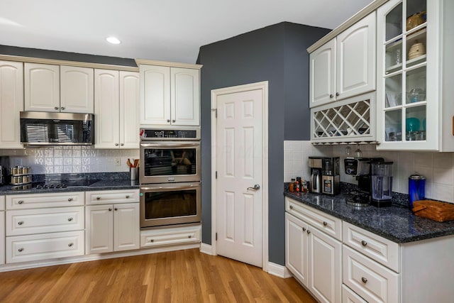 kitchen featuring appliances with stainless steel finishes, tasteful backsplash, light hardwood / wood-style flooring, and dark stone countertops