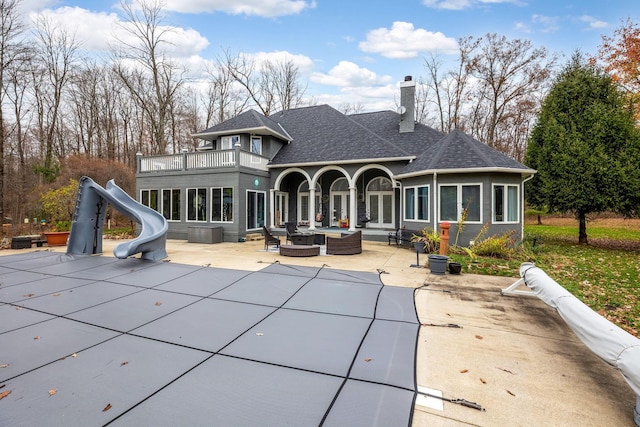 back of house featuring outdoor lounge area, a balcony, a patio, and a covered pool