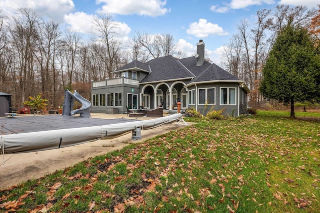 view of front facade with a balcony, a front lawn, an outdoor living space, a patio, and a covered pool