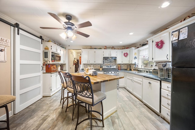 kitchen with white cabinetry, a barn door, stainless steel gas range oven, black fridge, and light hardwood / wood-style floors