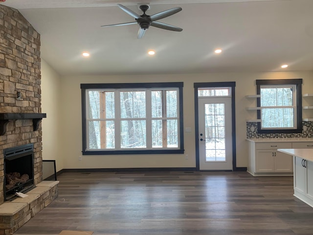 unfurnished living room with dark hardwood / wood-style flooring, a stone fireplace, ceiling fan, and lofted ceiling