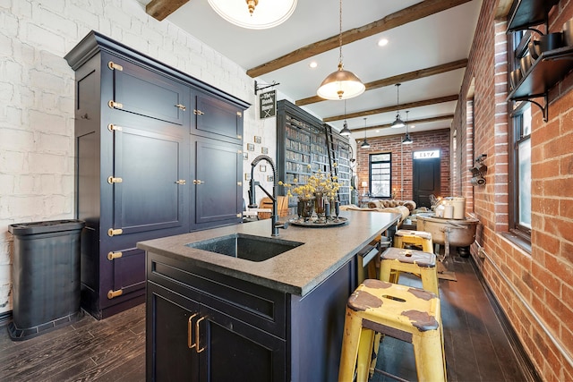 kitchen featuring beamed ceiling, hanging light fixtures, brick wall, and sink