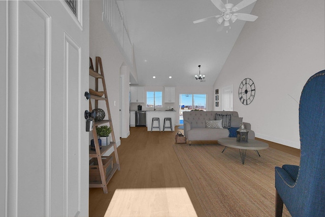 living room with high vaulted ceiling, ceiling fan with notable chandelier, and light hardwood / wood-style flooring