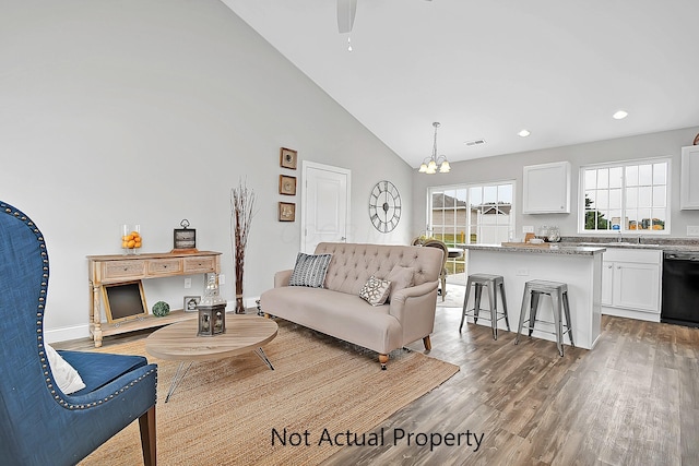 living room with high vaulted ceiling, wood-type flooring, sink, and ceiling fan with notable chandelier