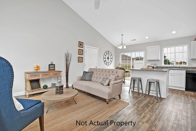 living room featuring ceiling fan with notable chandelier, sink, wood-type flooring, and high vaulted ceiling